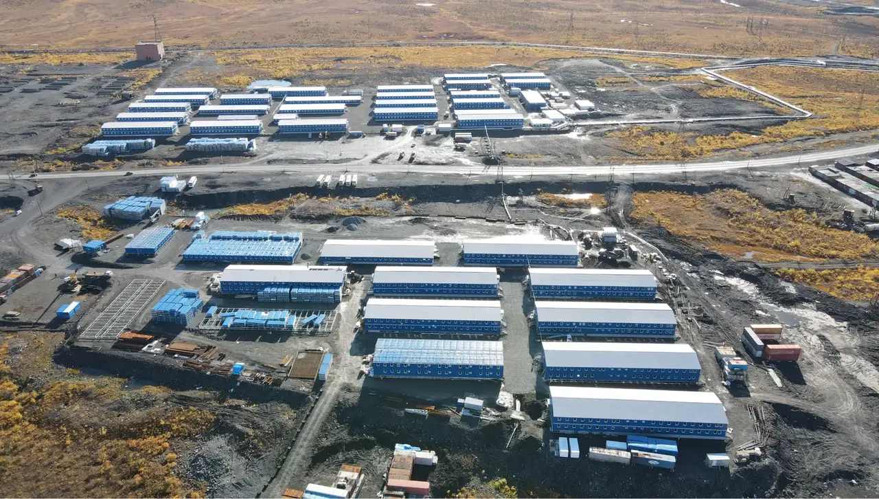 野外营地鸟瞰：两排两层住宿楼、模块堆场和安装作业区